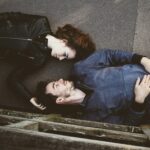 man and woman lying on gray concrete surface looking at each other